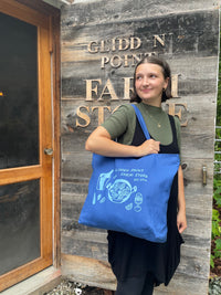 Person holding a blue tote bag with a logo in front of a wooden sign saying Glidden Point