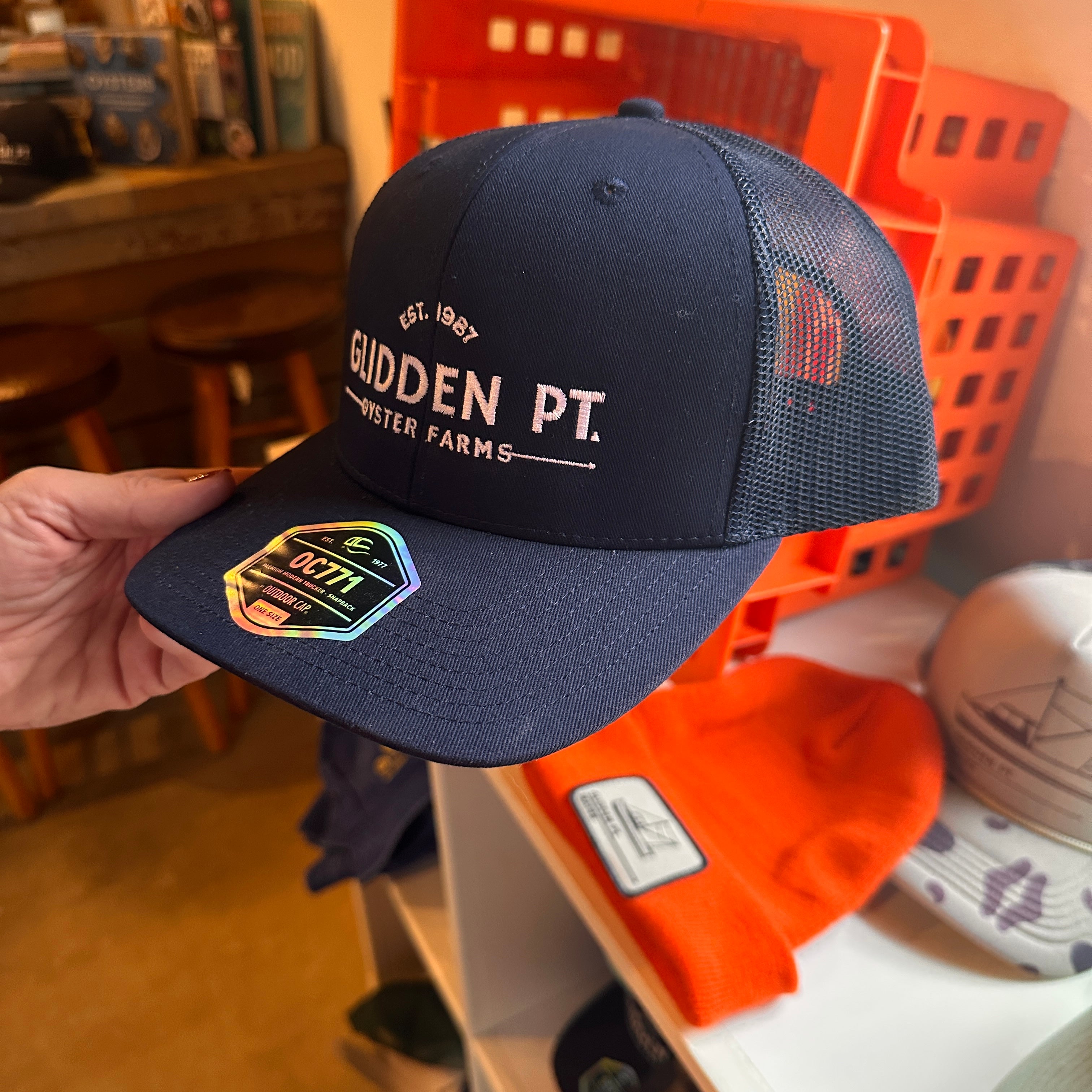 Navy blue cap with 'Glidden Pt.' branding held by a hand against a casual indoor background.