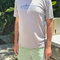 A man wearing a light gray heather crewneck t-shirt with a blue boat graphic and pale green shorts, standing on a wooden deck outdoors.