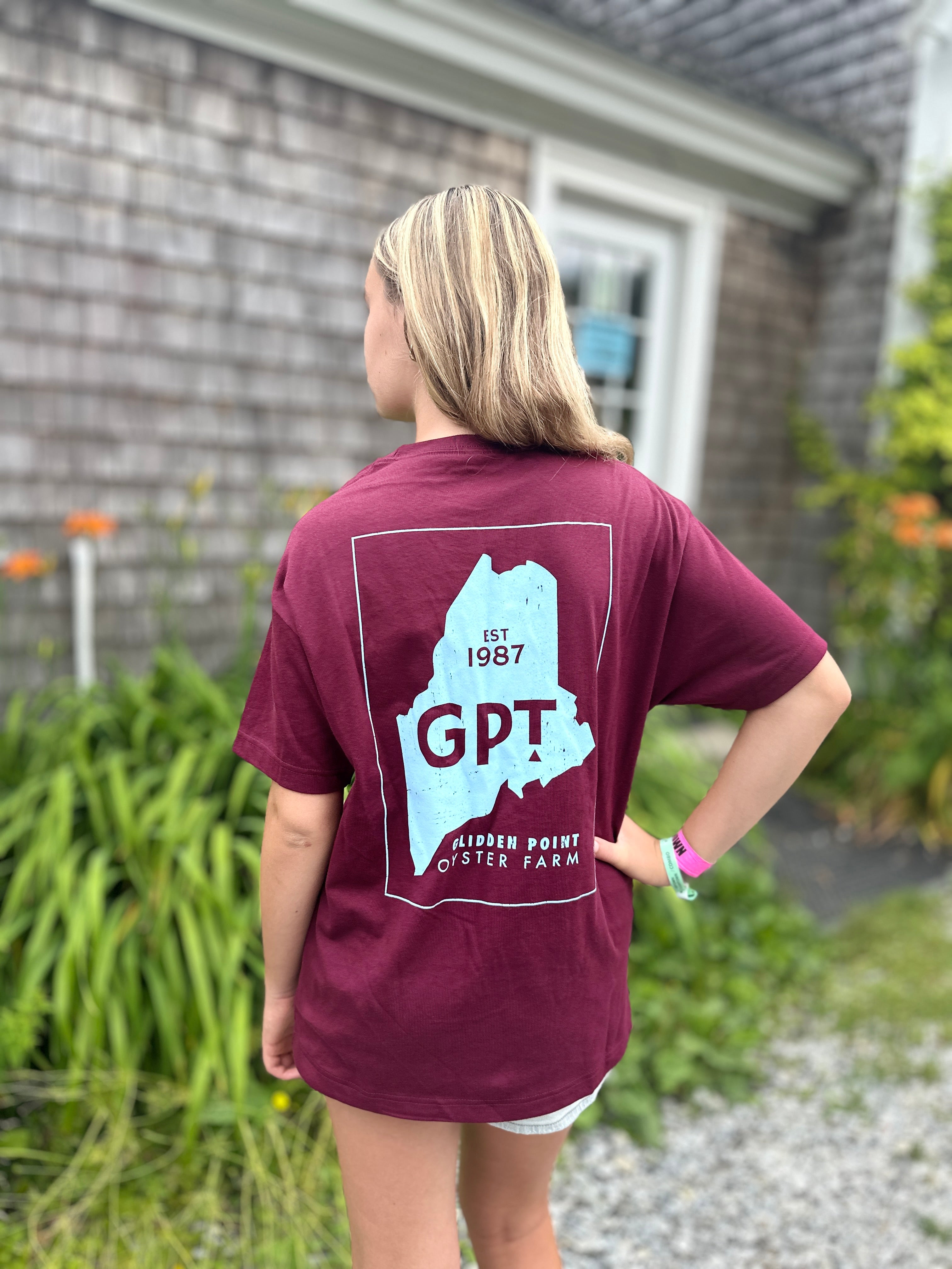 Person wearing a maroon t-shirt with 'GPT' and a map design, standing outdoors.