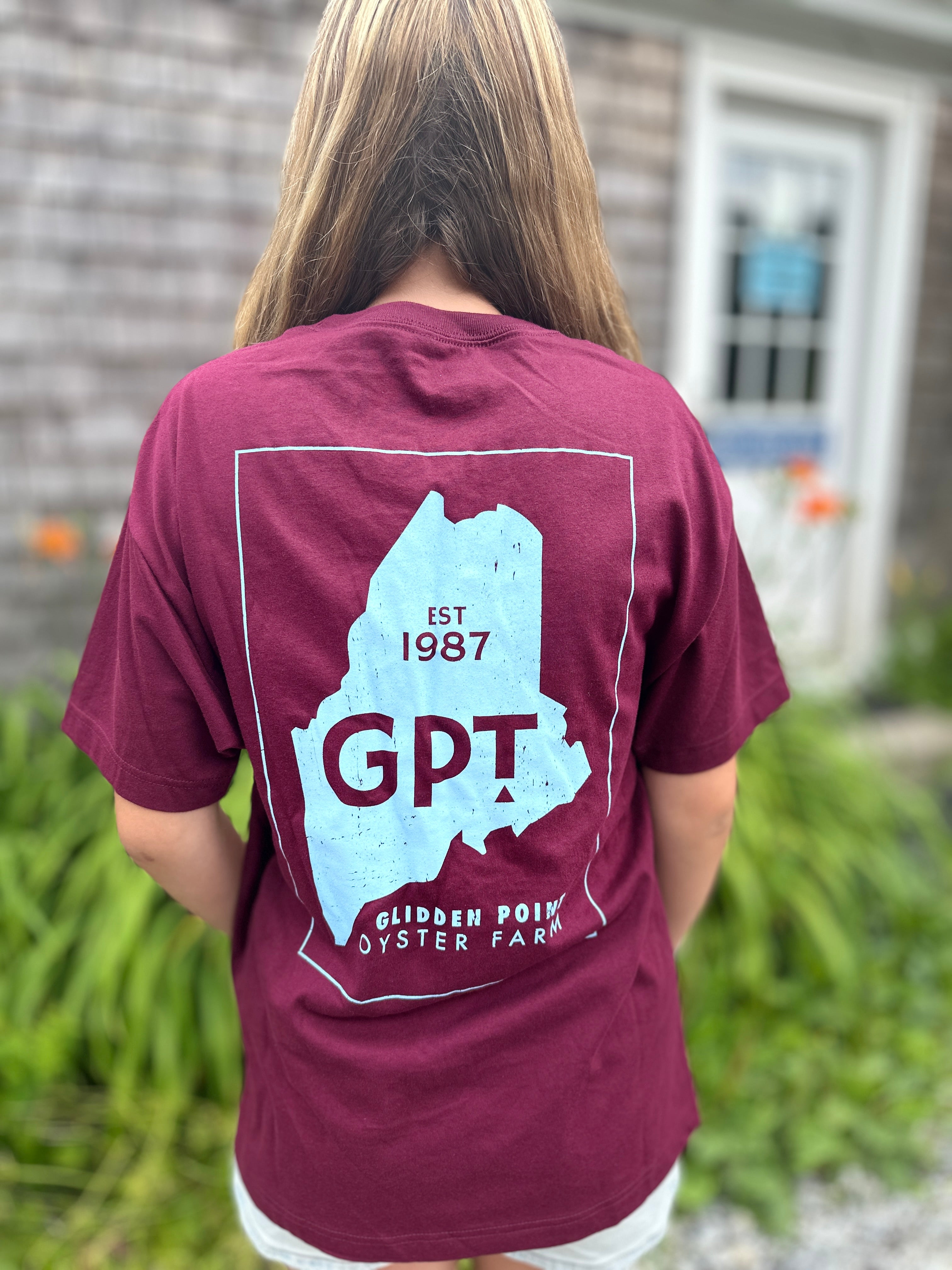 Person wearing a maroon t-shirt with a graphic design on the back, standing outdoors.